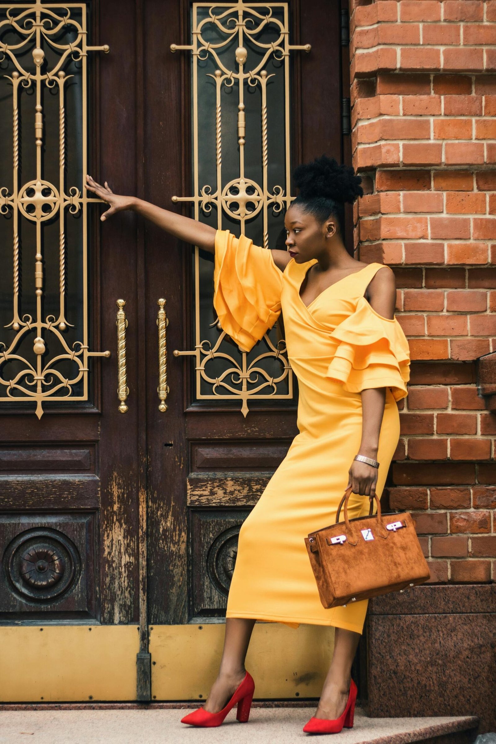 Elegant black woman in yellow dress and red heels posing by a decorative door.